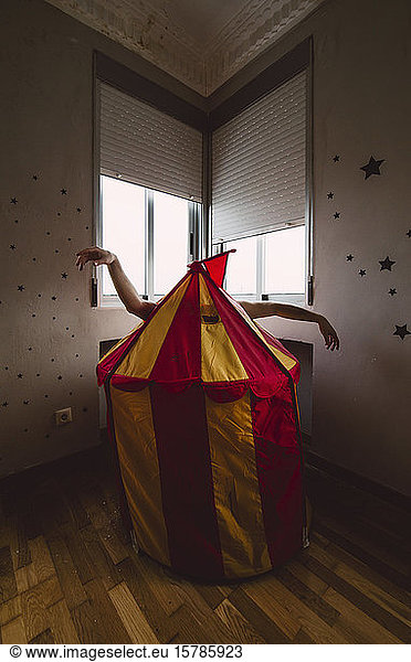 Person hiding behind toy tent in empty room