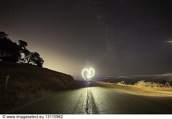 Person making heart shape while performing light painting on mountain road at night