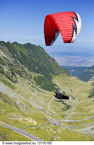 Person paragliding above mountains against clear sky