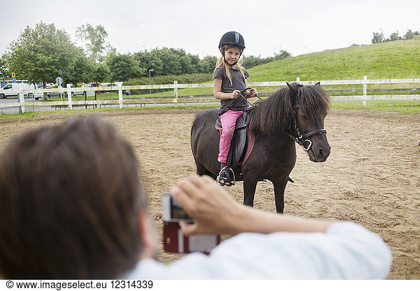 Person photographing girl (4-5) on pony