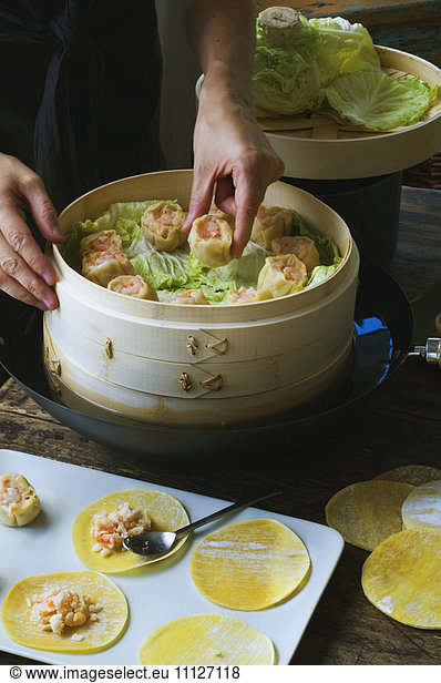 Person putting Asian dumplings in steamer with cabbage