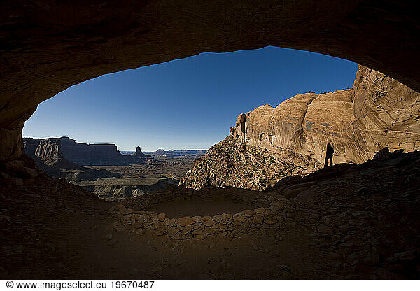Person standing in alcove near indian ruin with view of desert  Canyonlands National Park  Utah.