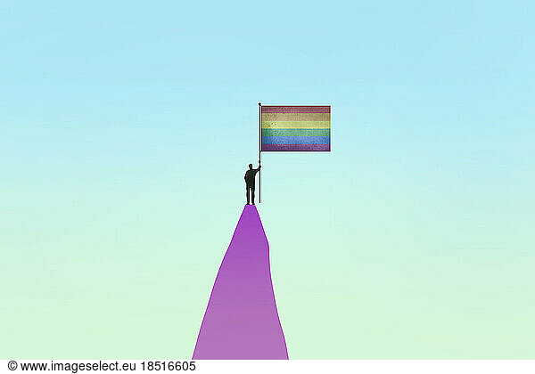 Person standing with rainbow flag on top of mountain peak