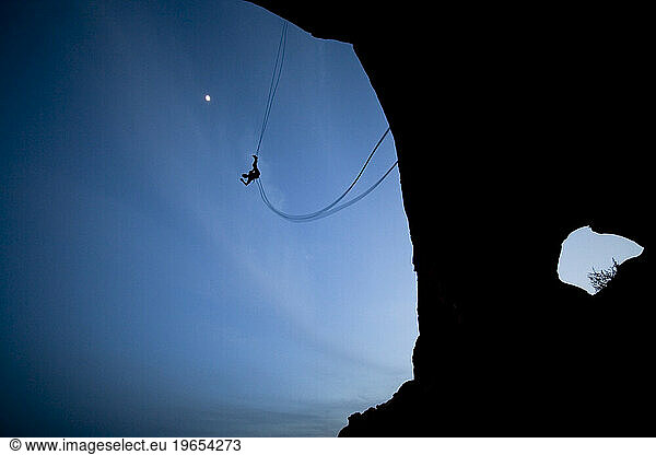 Person swinging on a rope swing off of a rock formation near Moab  Utah.