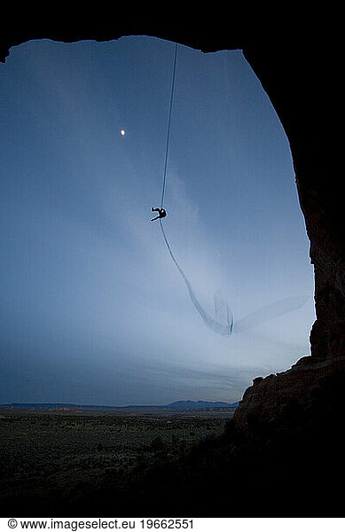 Person swinging on a rope swing off of a rock formation near Moab  Utah.