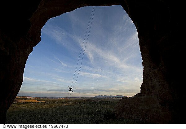 Person swinging on a rope swing off of a rock formation near Moab  Utah.