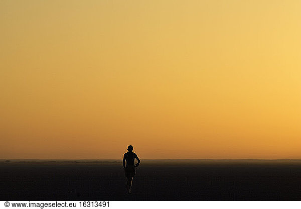 Person walking across the Makadikadi Salt Pans in Botswana  at sunset.