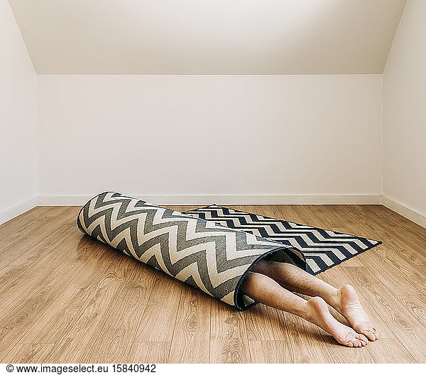 person with bare feet rolled up inside carpet on floor in empty room