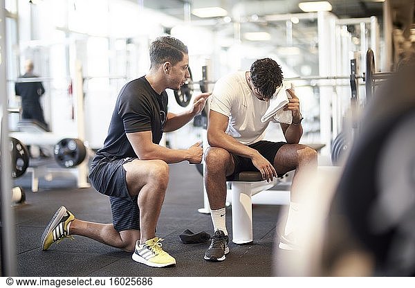 Personal Trainer  der einem Mann beim Training im Fitnessstudio hilft