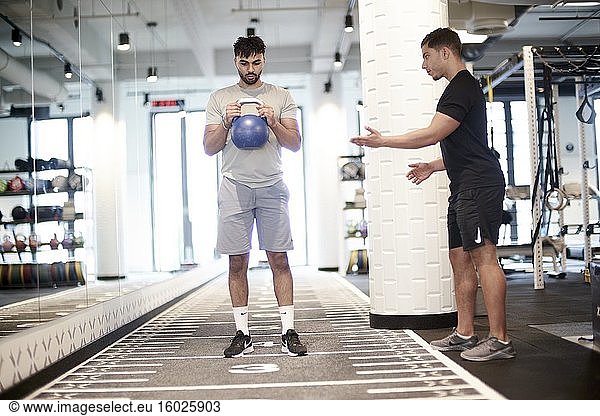 Personal Trainer  der einem Mann beim Training im Fitnessstudio hilft