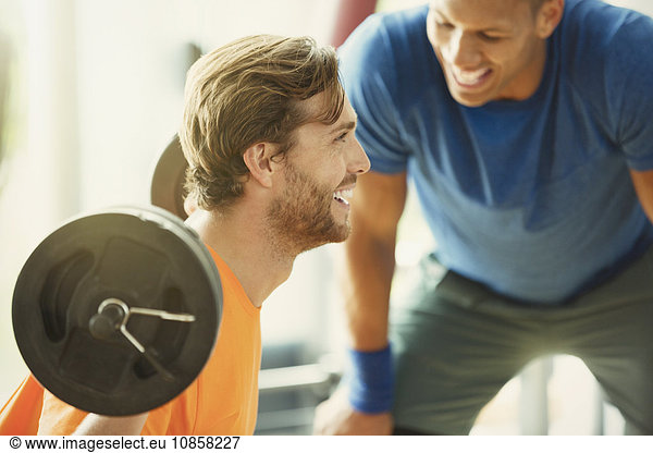 Personal trainer encouraging man doing barbell squats at gym