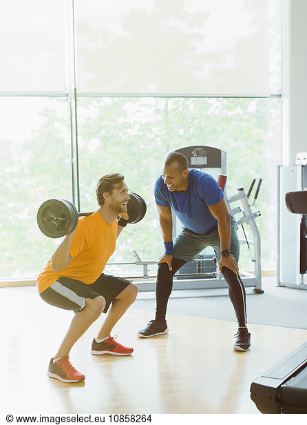Personal trainer guiding man doing barbell squats at gym