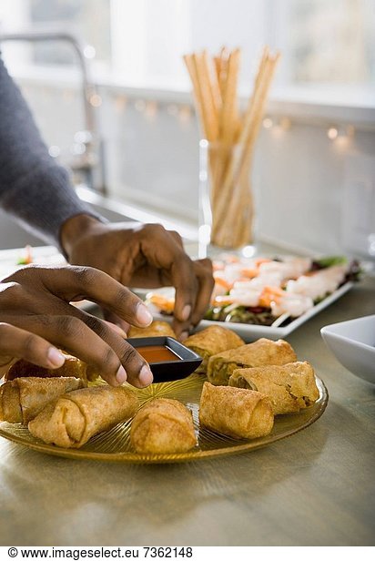 Persons hand putting a dip on a plate of spring rolls