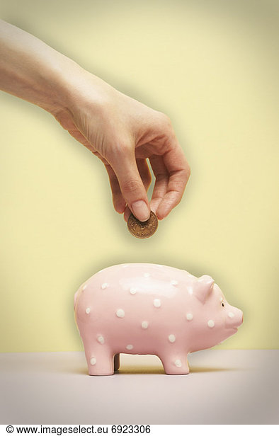 Persons Hand Putting Coin in Piggy Bank