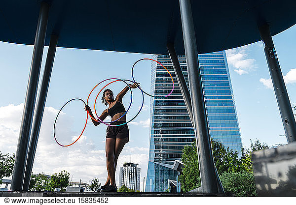 Perspective view of young woman dancing with four Hula Hoop in city