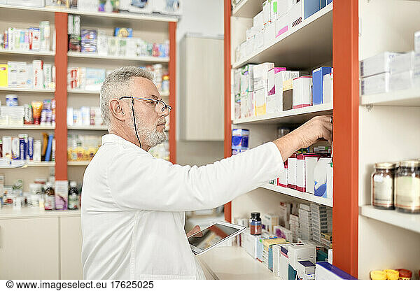 Pharmacist holding tablet PC stacking medicine on shelf at pharmacy store