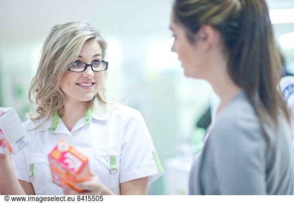 Pharmacist talking to customer  holding boxes of vitamins