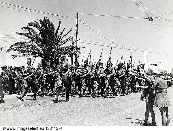 Photograph of two children waving as French troops march along Avenue Gambetta  during the allied victory parade  Tunis  Tunisia. Dated 1943