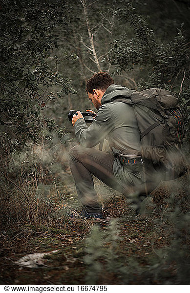 Photographer looks at camera camouflaged between bushes on nature