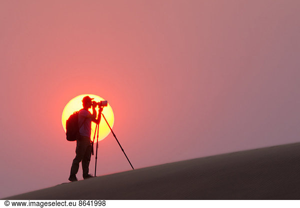 Photographer silhouetted in the setting sun in the Namib Desert  Namibia