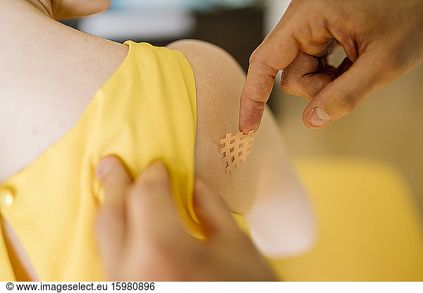 Physiotherapist applying cross tape on patient's shoulder