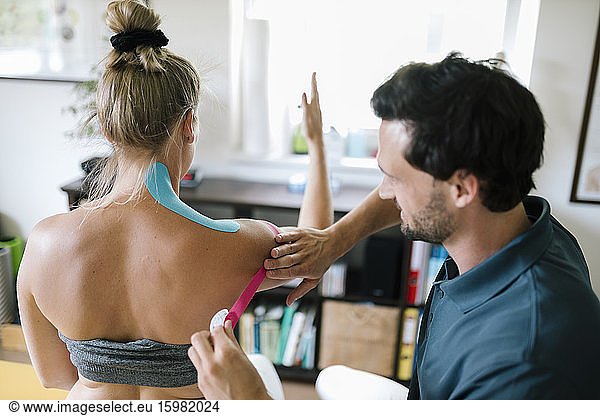Physiotherapist applying therapeutic tape on patient's neck and shoulder