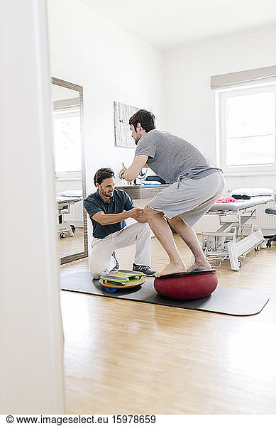 Physiotherapist assisting patient  practicing on balance trainer