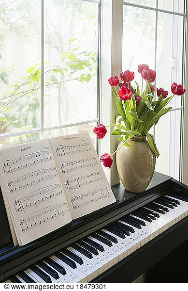 Piano with bouquet of tulips and music sheets in living room at home