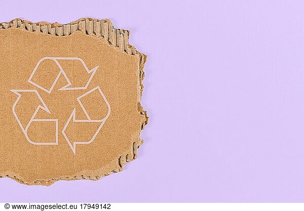 Piece of cardboard with recycling arrow sign on violet blue background with copy space