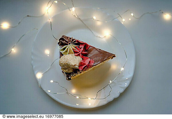 Piece of homemade chocolate cake on a white plate among lights. View f