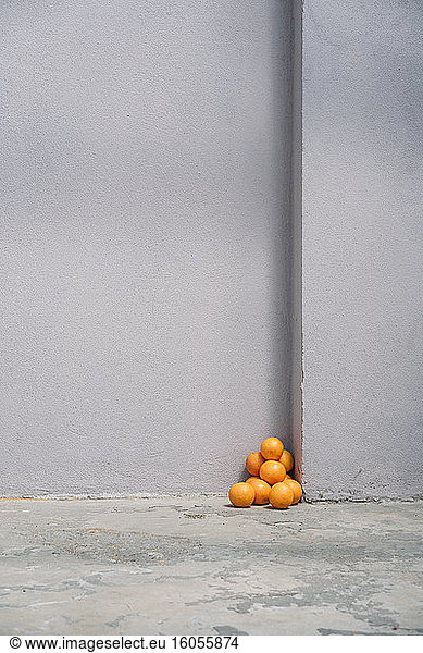 Pile of oranges in corner of a gray wall