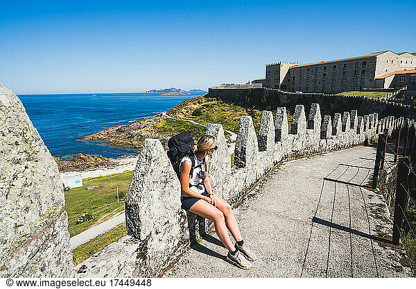 pilgrim woman sitting on the wall of a castle against the sea