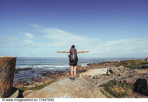 pilgrim woman with open arms on top of a rock looking at the horizon