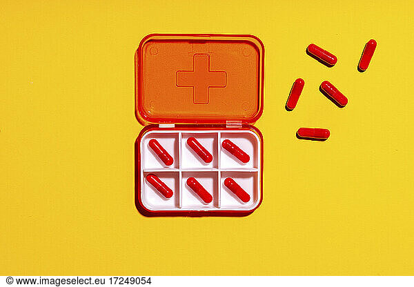 Pill box with red capsules against yellow background