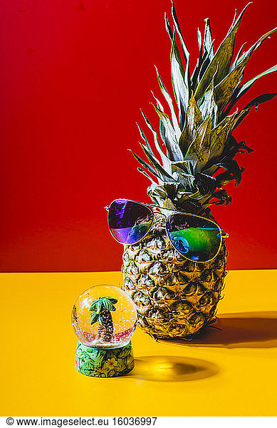 Pineapple with sunglasses in front of a snow globe with a mini palm tree