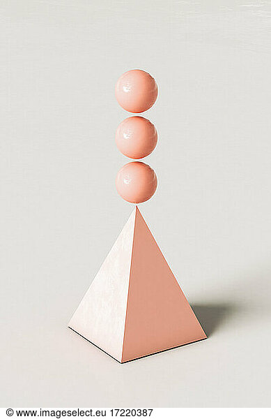 Pink abstract pyramid with three spheres balancing on top against cream colored background
