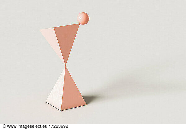 Pink abstract pyramids with a sphere balancing on top against cream colored background