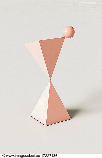 Pink abstract pyramids with a sphere balancing on top over cream colored background