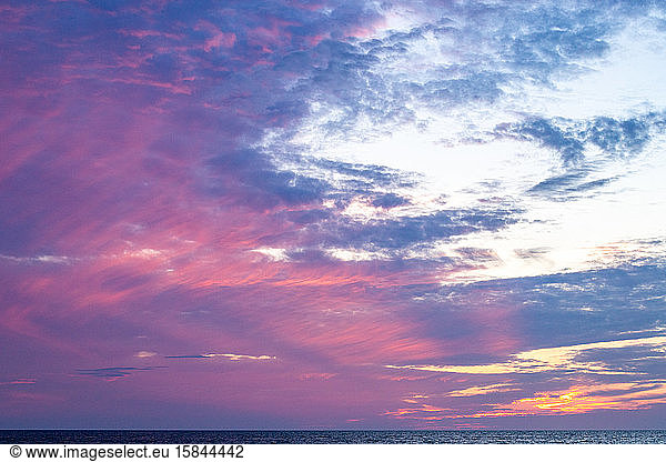 Pink clouds filling the sky above the ocean during sunset.