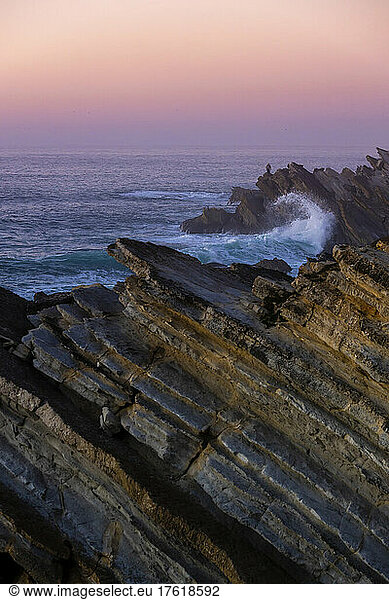 Pink glowing sunset sky over the Atlantic Ocean and the rugged rocks lining the coastline at Praia Baleal; Peniche  Oeste  Portugal