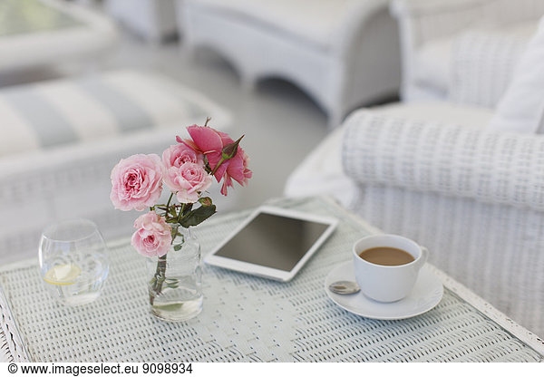 Pink roses on patio table with coffee cup and digital tablet