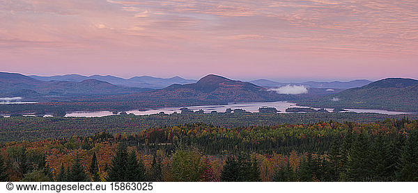 Pink sky at sunrise over mountains and a lake in fall in Maine