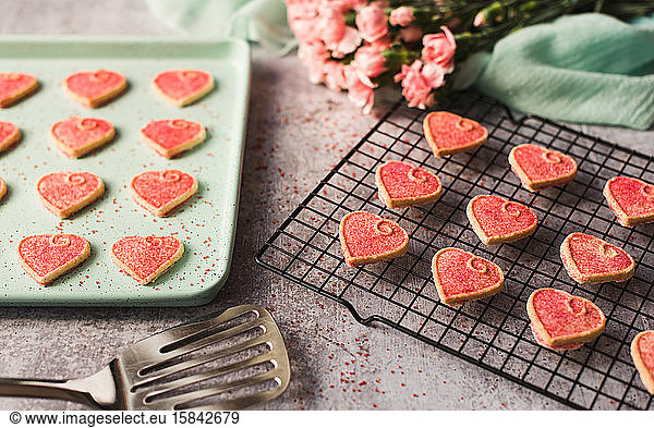 Pink Valentine's day heart cookies cooling on a pan and rack.