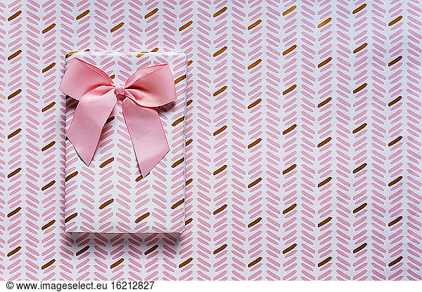 Pink wrapped gift against wrapping paper background