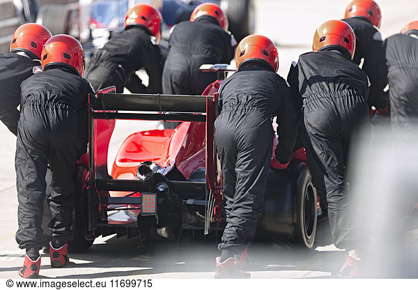 Pit crew pushing formula one race car out of pit lane