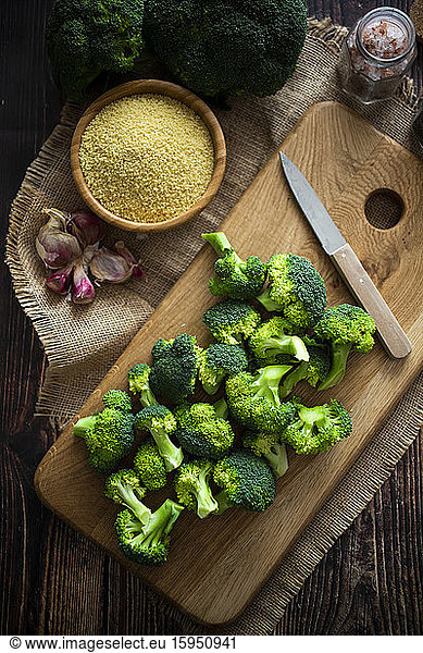 Place mat  cutting board  salt  garlic  bowl of couscous  kitchen knife and fresh broccoli