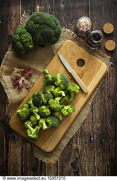 Place mat  salt and pepper  cutting board  kitchen knife  garlic  and fresh broccoli