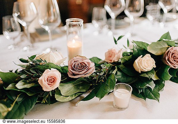 Place setting at wedding reception table with rose garland decoration  candles and drinking glasses