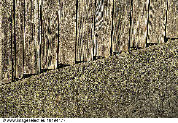 Planks of a wooden fence and concrete wall.