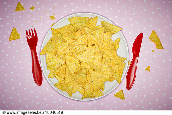 Plate of cheese nachos and red plastic cutlery on pink cloth